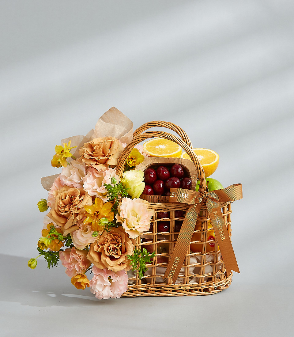 Citrus fruit and flower basket with fresh oranges, cherries, and a bouquet of peach and yellow flowers.
