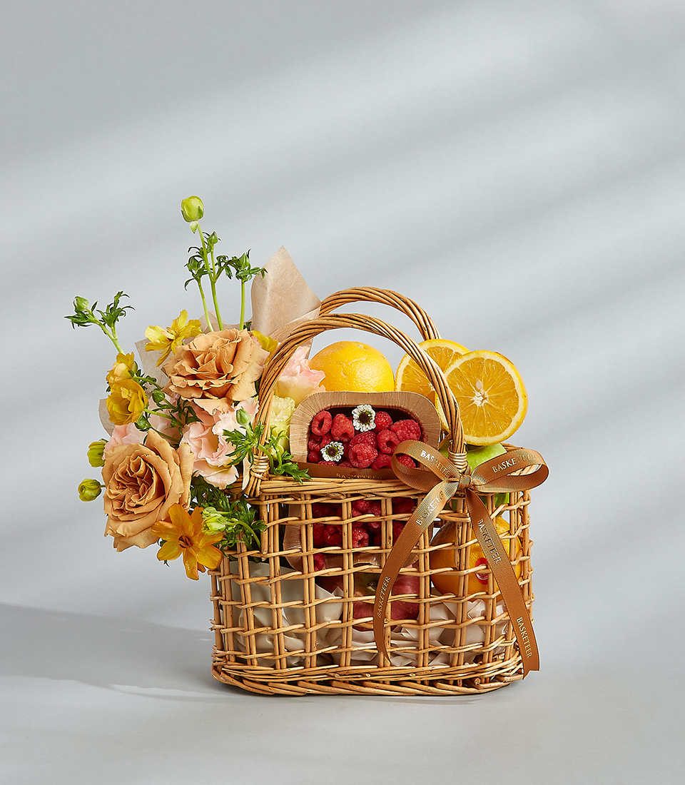 Citrus and berry gift basket with fresh oranges, raspberries, and a bouquet of peach and yellow flowers.