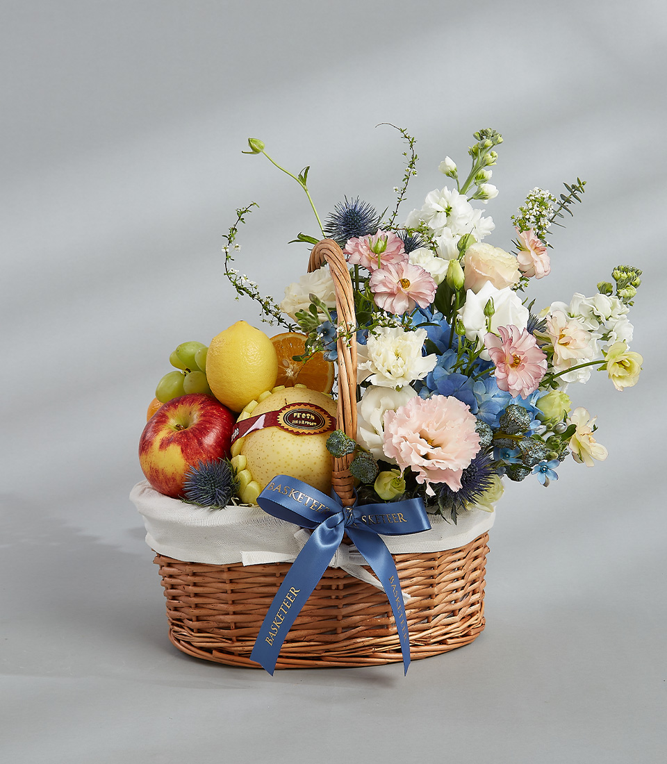 Pastel flower and fruit basket with fresh apples, grapes, pears, and a bouquet of pastel-colored flowers.