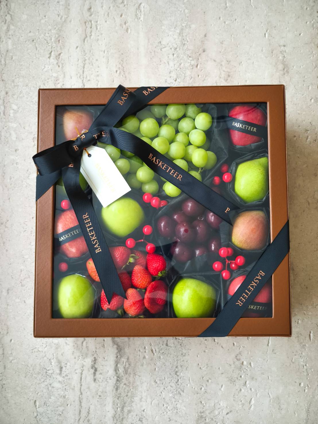 Luxury fruit gift box with green grapes, apples, strawberries, red grapes, and elegant BASKETEER ribbon