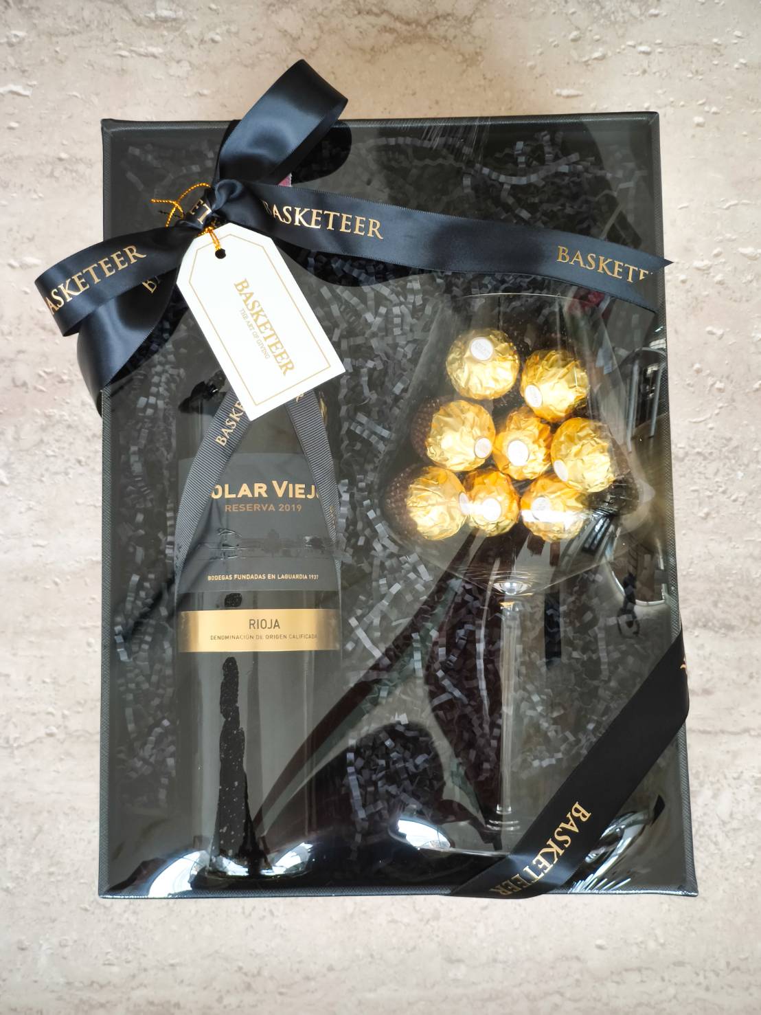 Black luxury gift box with Solar Viejo Rioja red wine, Ferrero Rocher chocolates, wine glass, and black ribbon