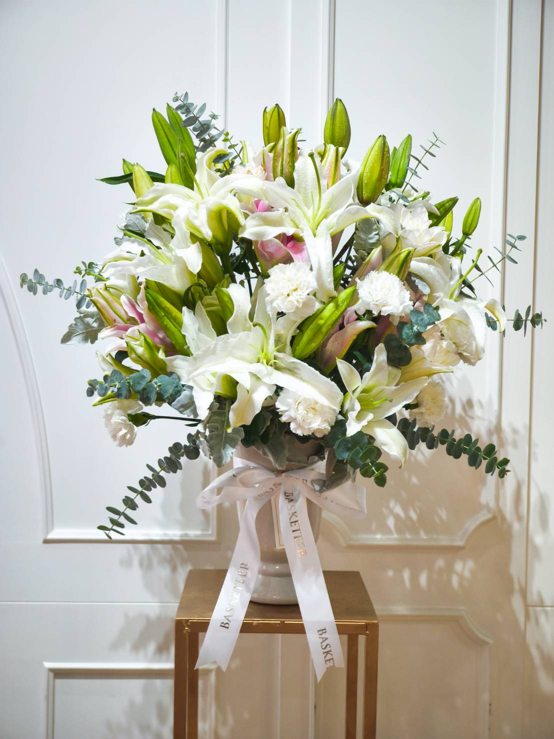 Elegant flower vase arrangement with white lilies, pink lilies, white carnations, and eucalyptus in a ceramic vase with ribbon