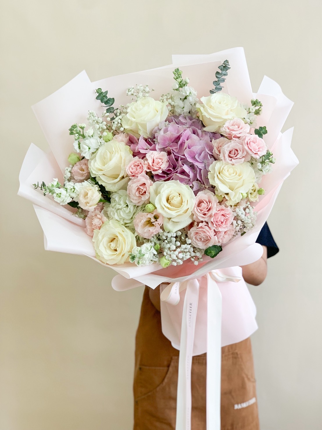 Luxury bouquet of pastel roses, pink hydrangeas, baby’s breath, and mixed florals wrapped in soft pink paper.