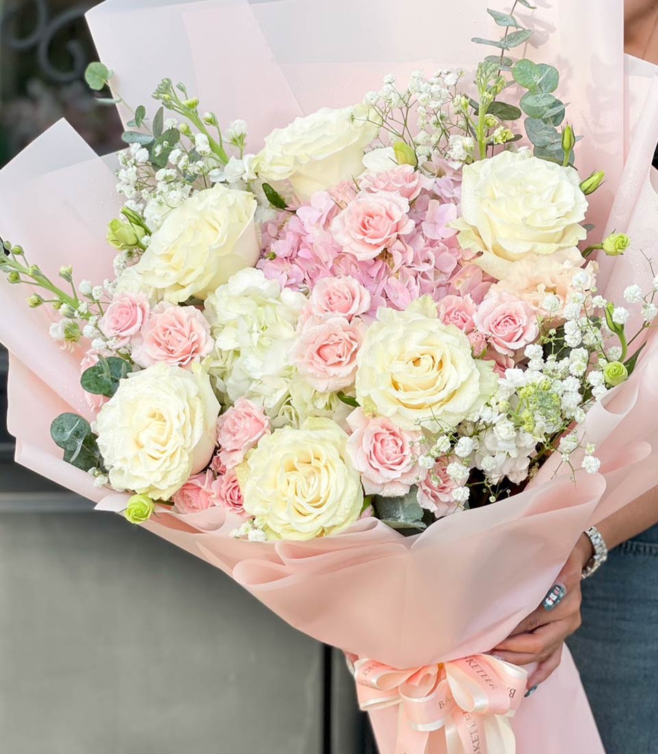 A stunning bouquet of soft pink and white roses, wrapped in pastel pink paper, accented with eucalyptus and baby's breath.