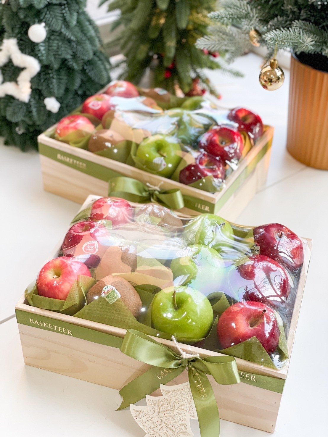 Premium fruit gift box with fresh red apples, green apples, kiwi, and a green festive ribbon in a wooden box.
