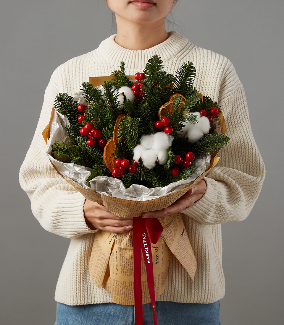 Christmas bouquet featuring fresh pine branches, red berries, and cotton, held by a person wearing a cream sweater.