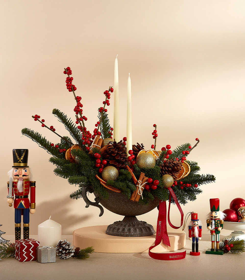 Holiday centerpiece with red berries, pinecones, golden ornaments, candles, and nutcracker figurines.