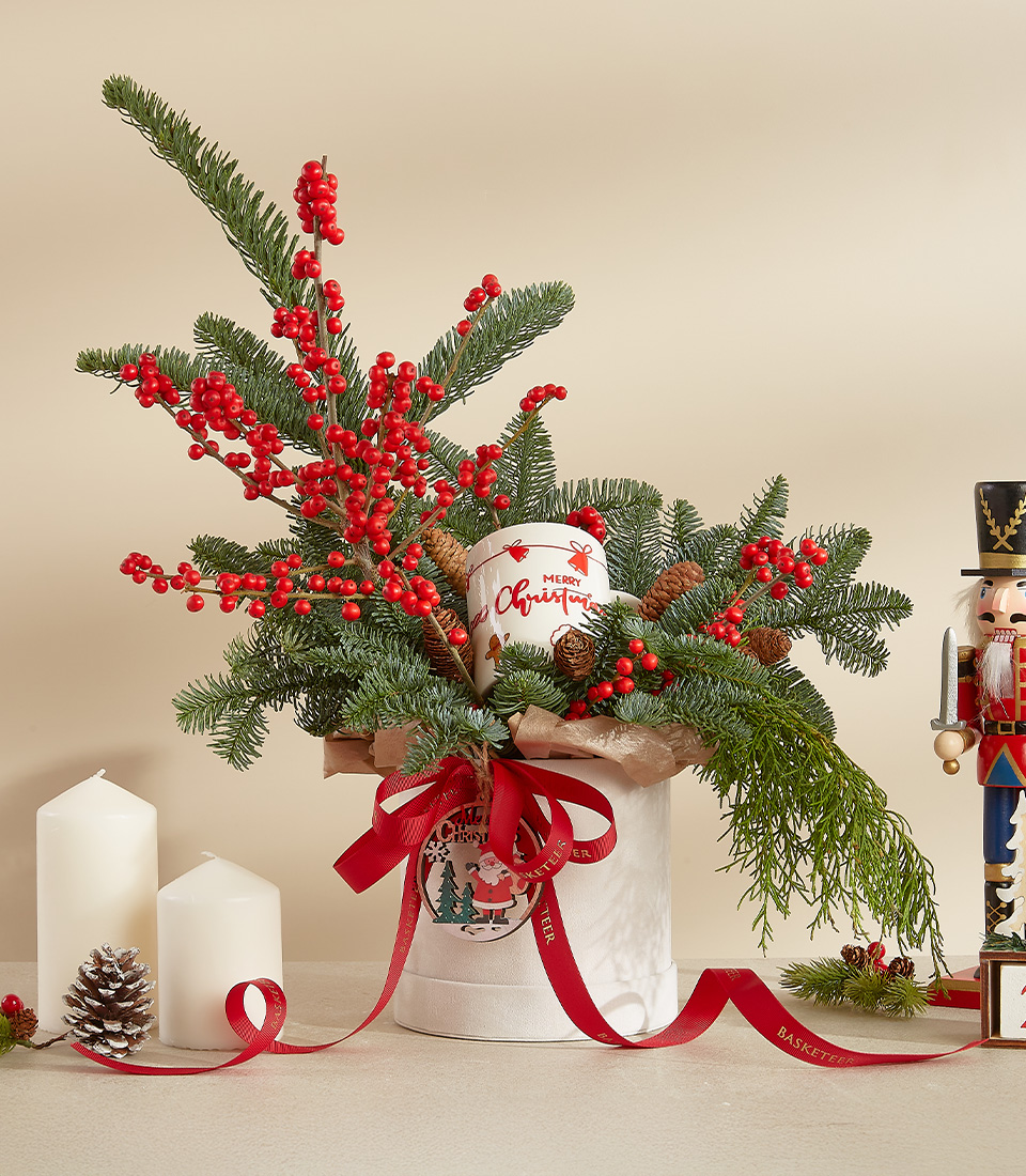 Festive holiday arrangement with red berries, pine branches, and red baubles in a decorative pot.