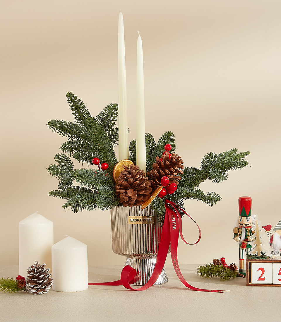 Christmas candle arrangement with white candles, pinecones, greenery, red berries, and dried orange slices in a silver vase.