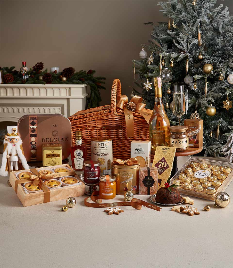 Deluxe Christmas hamper with Belgian chocolates, festive pastries, preserves, and holiday treats, arranged near a decorated Christmas tree.