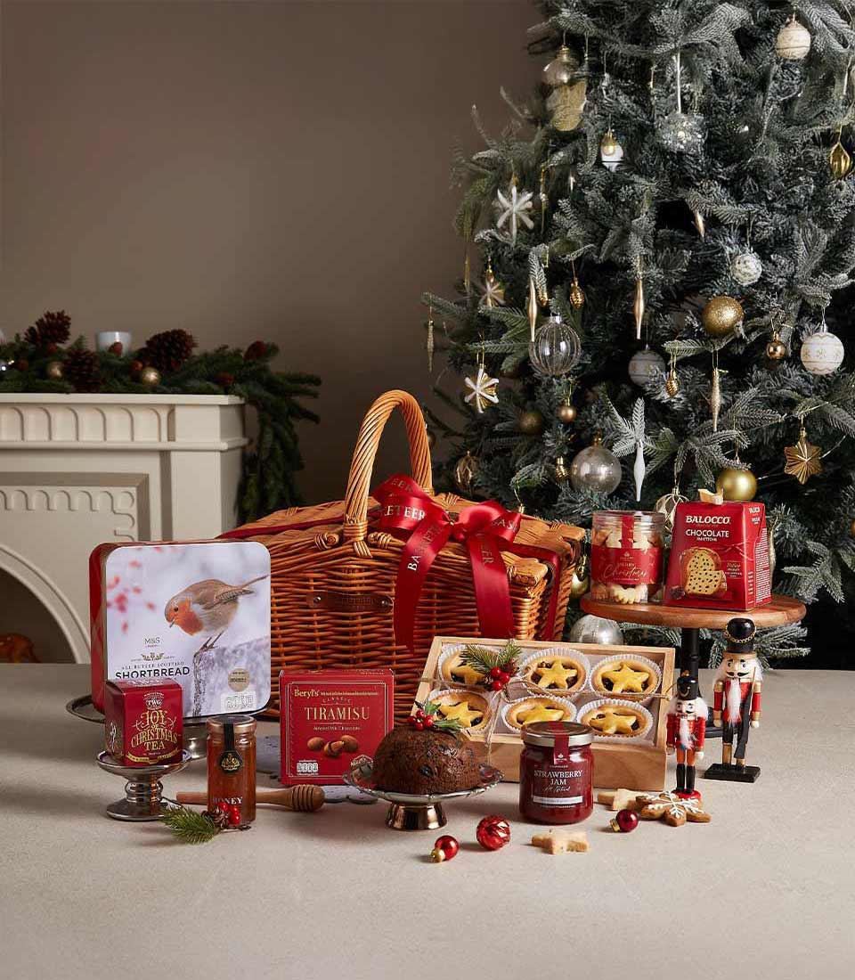 Traditional Christmas hamper with shortbread, tiramisu, pudding, and strawberry jam, displayed near a Christmas tree with festive decorations.