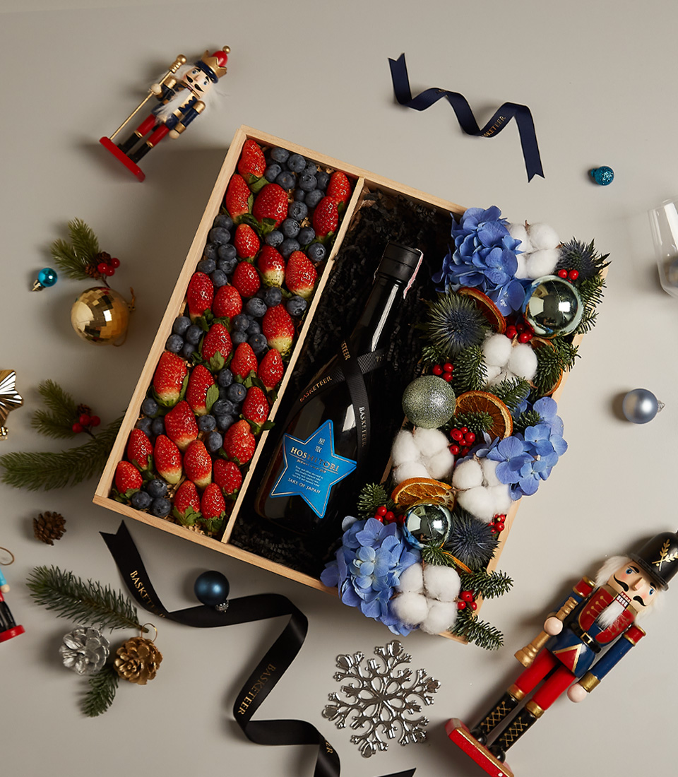 Festive gift box with strawberries, blueberries, and floral arrangements, accented with holiday decor.