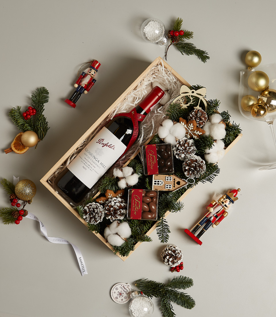 Christmas gift hamper featuring Penfolds wine, chocolates, gingerbread ornament, pinecones, and snowy decor.