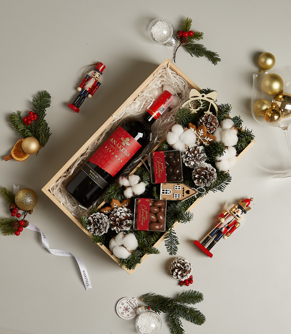 Christmas gift box with Anakena Merlot wine, chocolates, gingerbread ornament, pinecones, and festive decor.