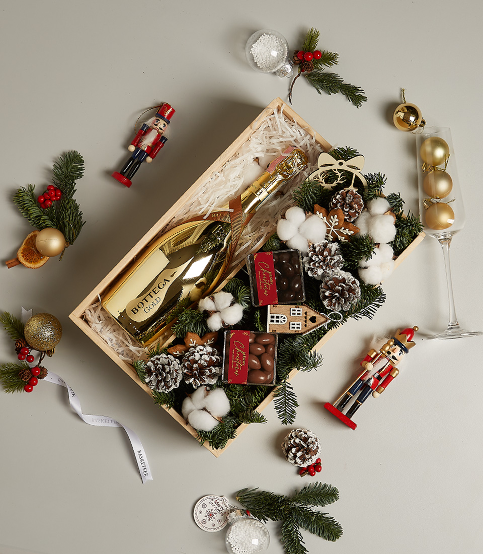 Christmas gift box with Bottega Gold Prosecco, chocolates, gingerbread ornament, pinecones, and festive holiday decor.