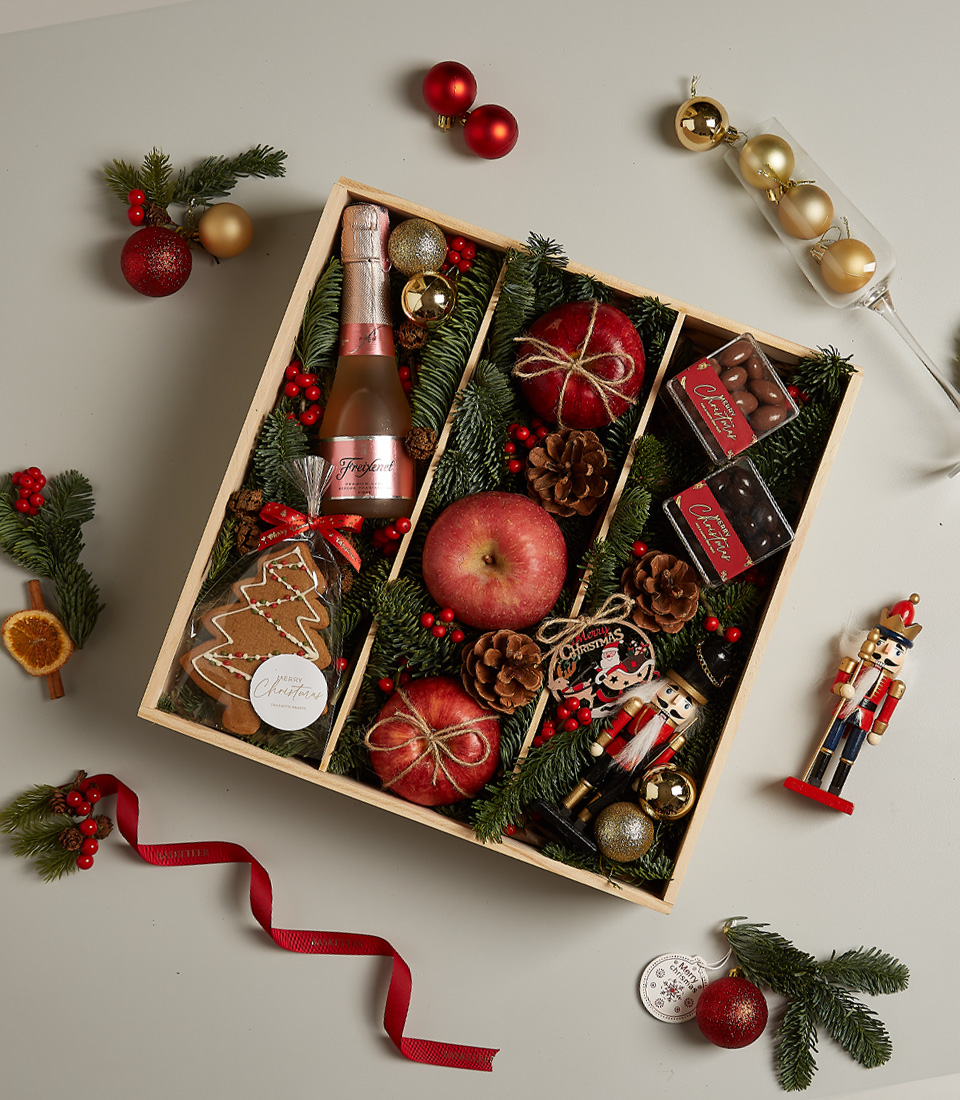 Christmas gift box with Freixenet Rosé, fresh apples, chocolates, gingerbread cookie, nutcracker, and festive holiday decor.