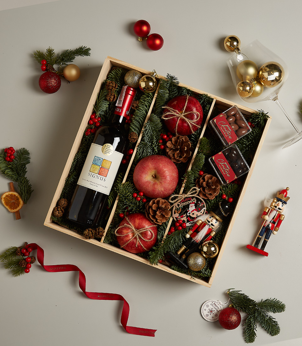Christmas gift box with Signus wine, fresh apples, chocolates, a nutcracker, and festive holiday decorations.