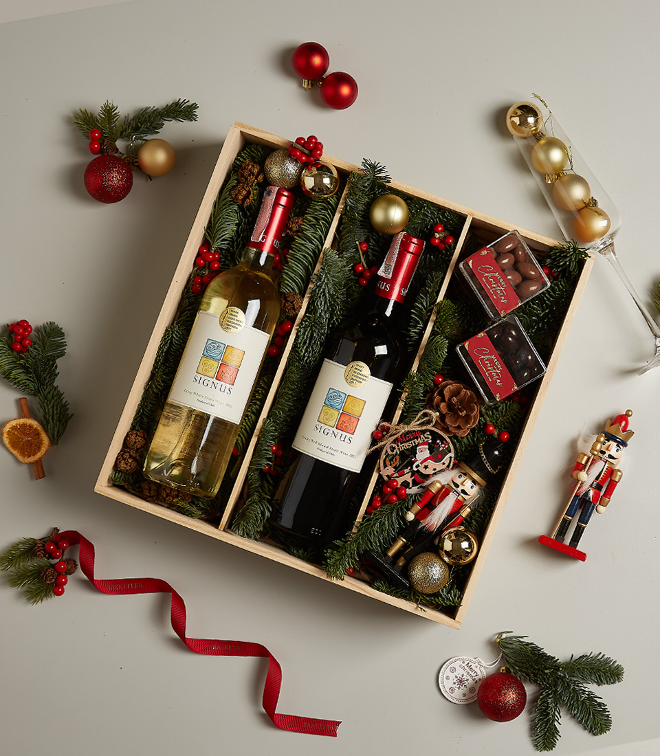 Christmas gift box with red and white Signus wines, chocolates, nutcracker, and holiday decorations.