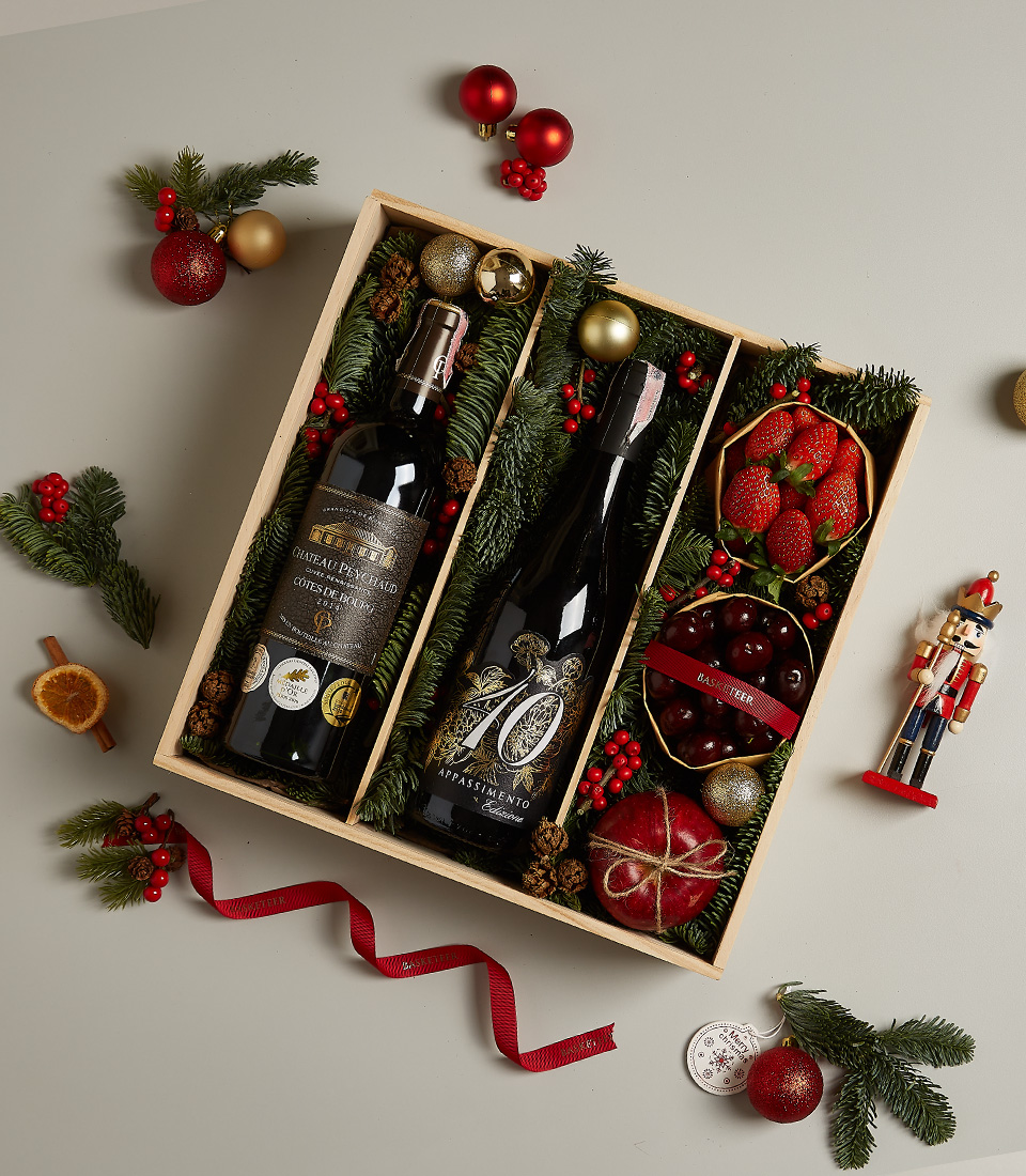 Holiday gift hamper featuring Château Peychaud red wine, Pasqua 10 Anniversario wine, fresh strawberries, cherries, and Christmas-themed decorations.
