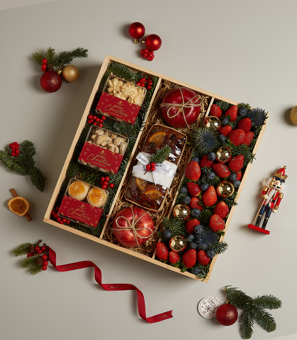 Christmas gift hamper with assorted cookies, fruitcake, fresh apples, strawberries, blueberries, and festive decorations.