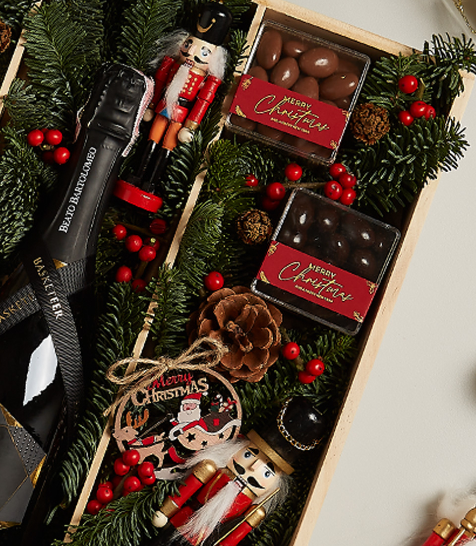 Deluxe holiday gift box with gingerbread, chocolates, festive ornaments, and seasonal greenery.