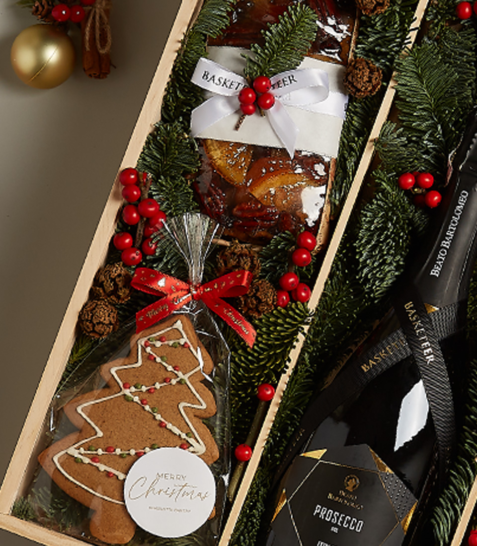 Deluxe holiday gift box with gingerbread, chocolates, festive ornaments, and seasonal greenery.