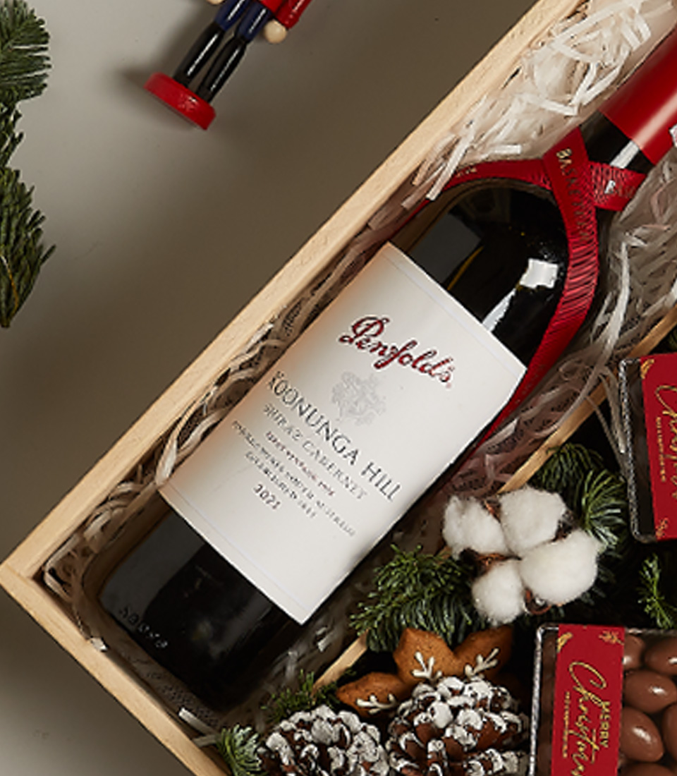 Christmas gift hamper featuring Penfolds wine, chocolates, gingerbread ornament, pinecones, and snowy decor.