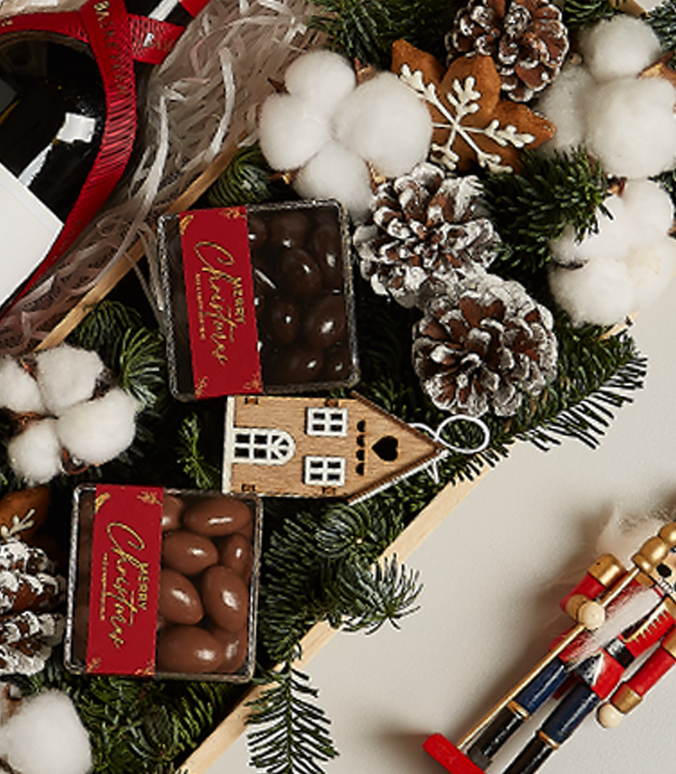 Christmas gift hamper featuring Penfolds wine, chocolates, gingerbread ornament, pinecones, and snowy decor.