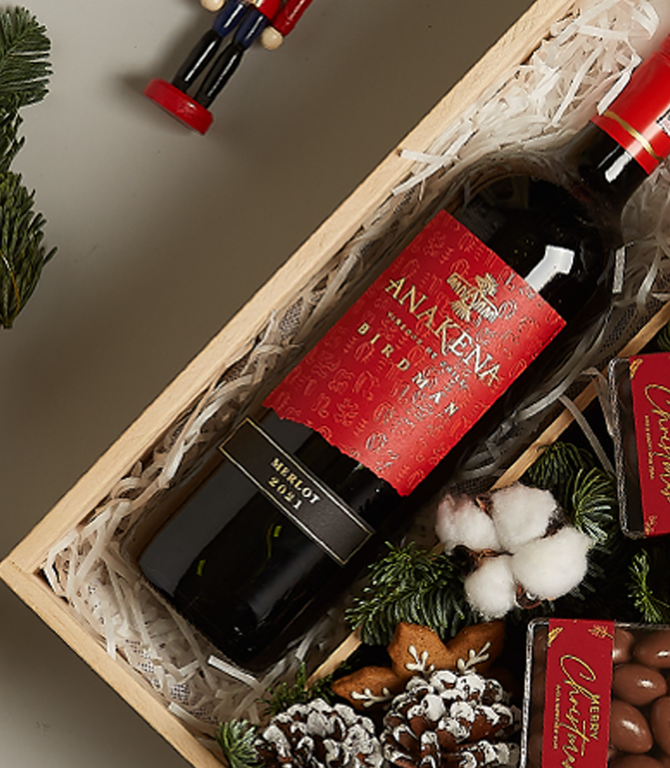 Christmas gift box with Anakena Merlot wine, chocolates, gingerbread ornament, pinecones, and festive decor.