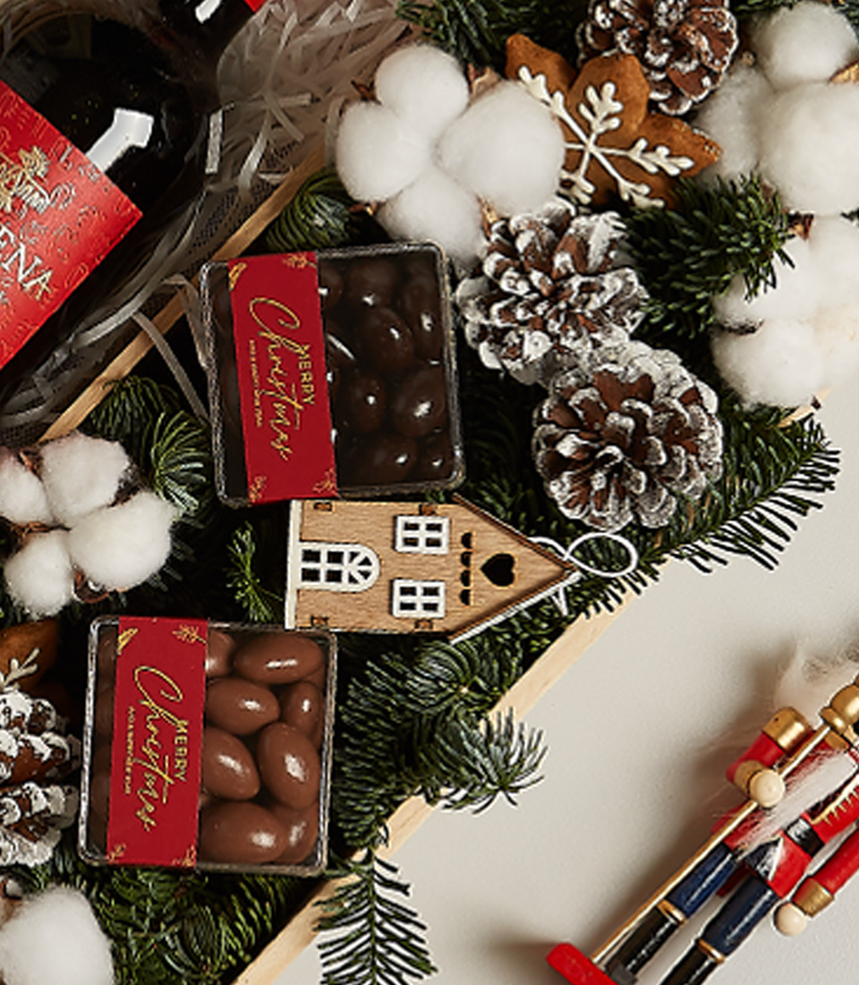 Christmas gift box with Anakena Merlot wine, chocolates, gingerbread ornament, pinecones, and festive decor.
