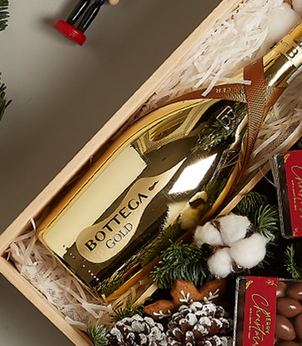 Christmas gift box with Bottega Gold Prosecco, chocolates, gingerbread ornament, pinecones, and festive holiday decor.