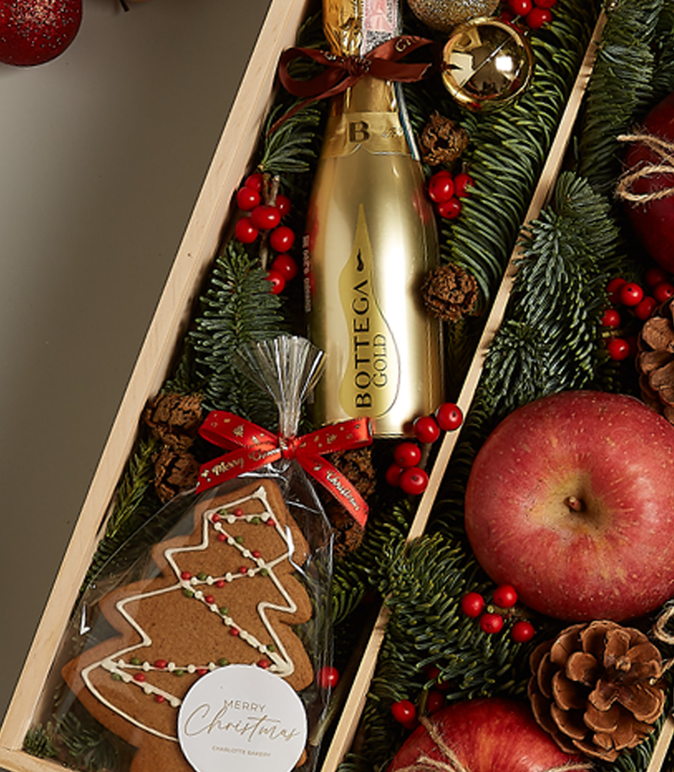 Christmas gift box featuring Bottega Gold Prosecco, apples, chocolates, gingerbread cookie, nutcracker, and festive holiday decor.