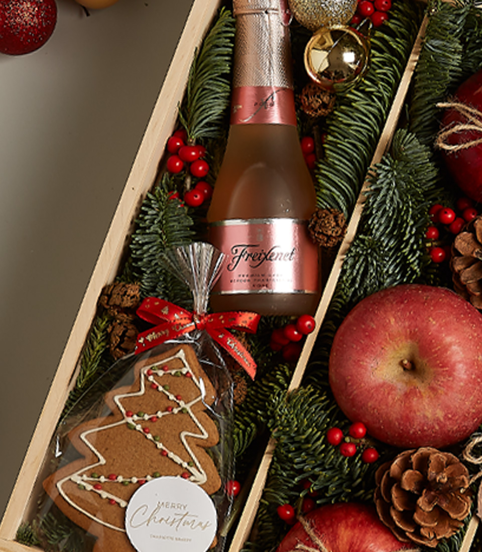 Christmas gift box with Freixenet Rosé, fresh apples, chocolates, gingerbread cookie, nutcracker, and festive holiday decor.