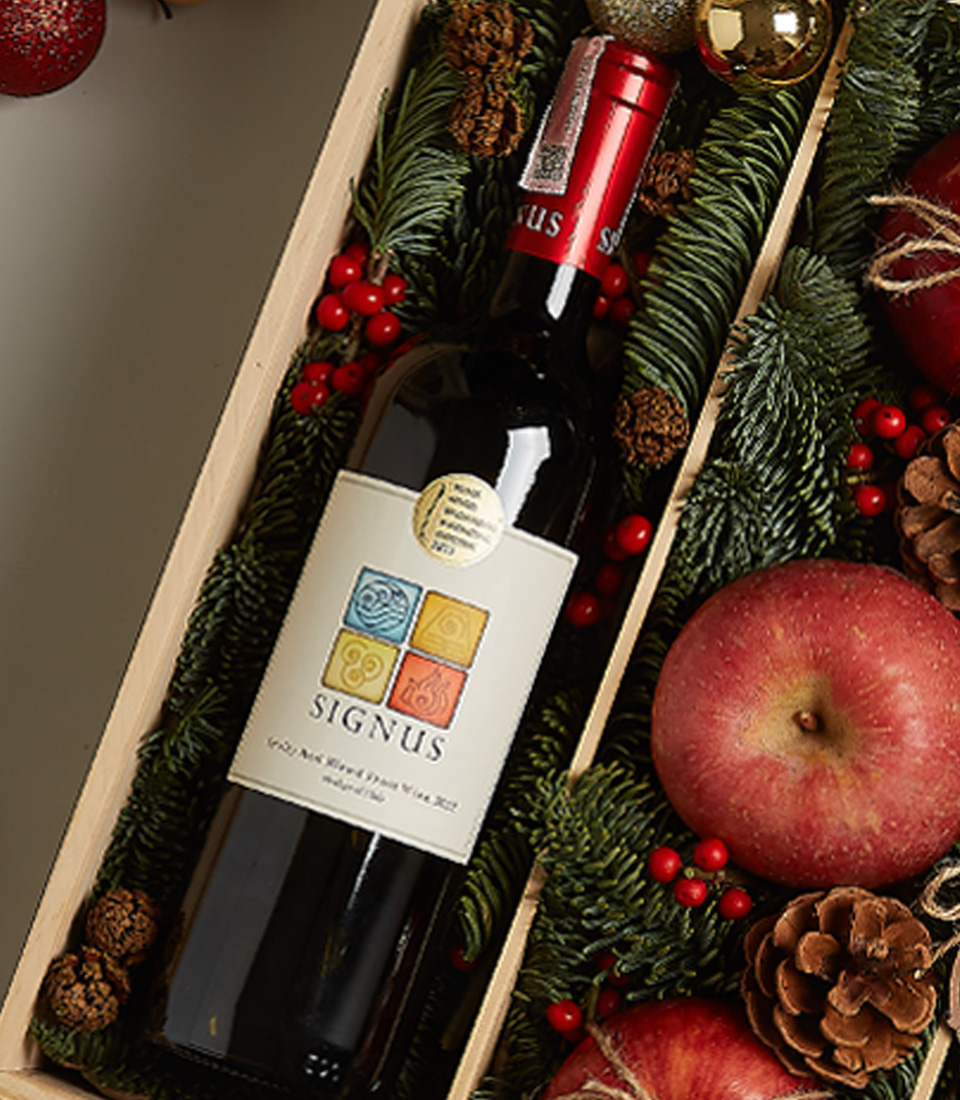Christmas gift box with Signus wine, fresh apples, chocolates, a nutcracker, and festive holiday decorations.