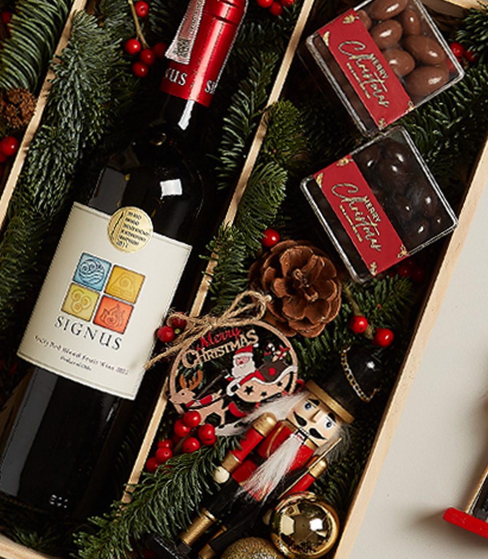 Christmas gift box with red and white Signus wines, chocolates, nutcracker, and holiday decorations.