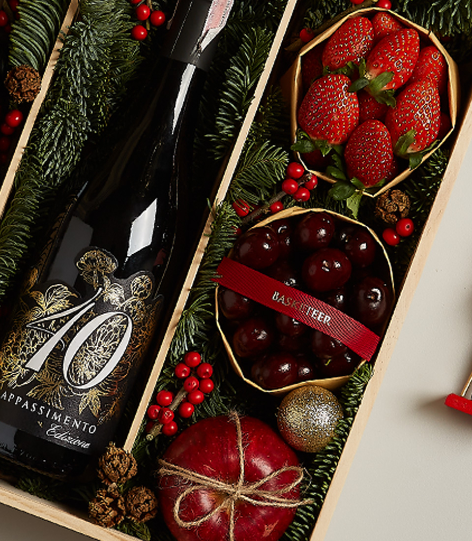 Holiday gift hamper featuring Château Peychaud red wine, Pasqua 10 Anniversario wine, fresh strawberries, cherries, and Christmas-themed decorations.