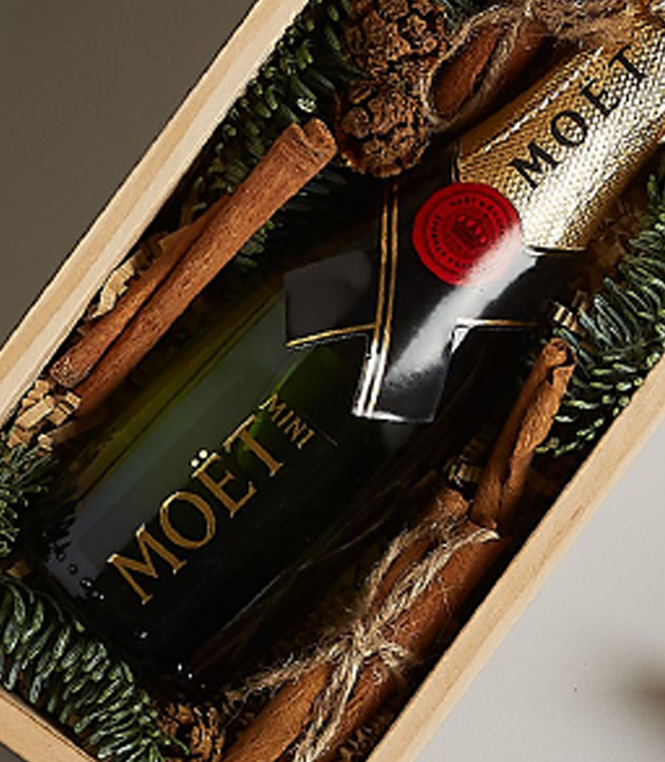 Holiday gift box with Moët & Chandon, gingerbread cookies, pinecones, and cinnamon sticks in a wooden container.