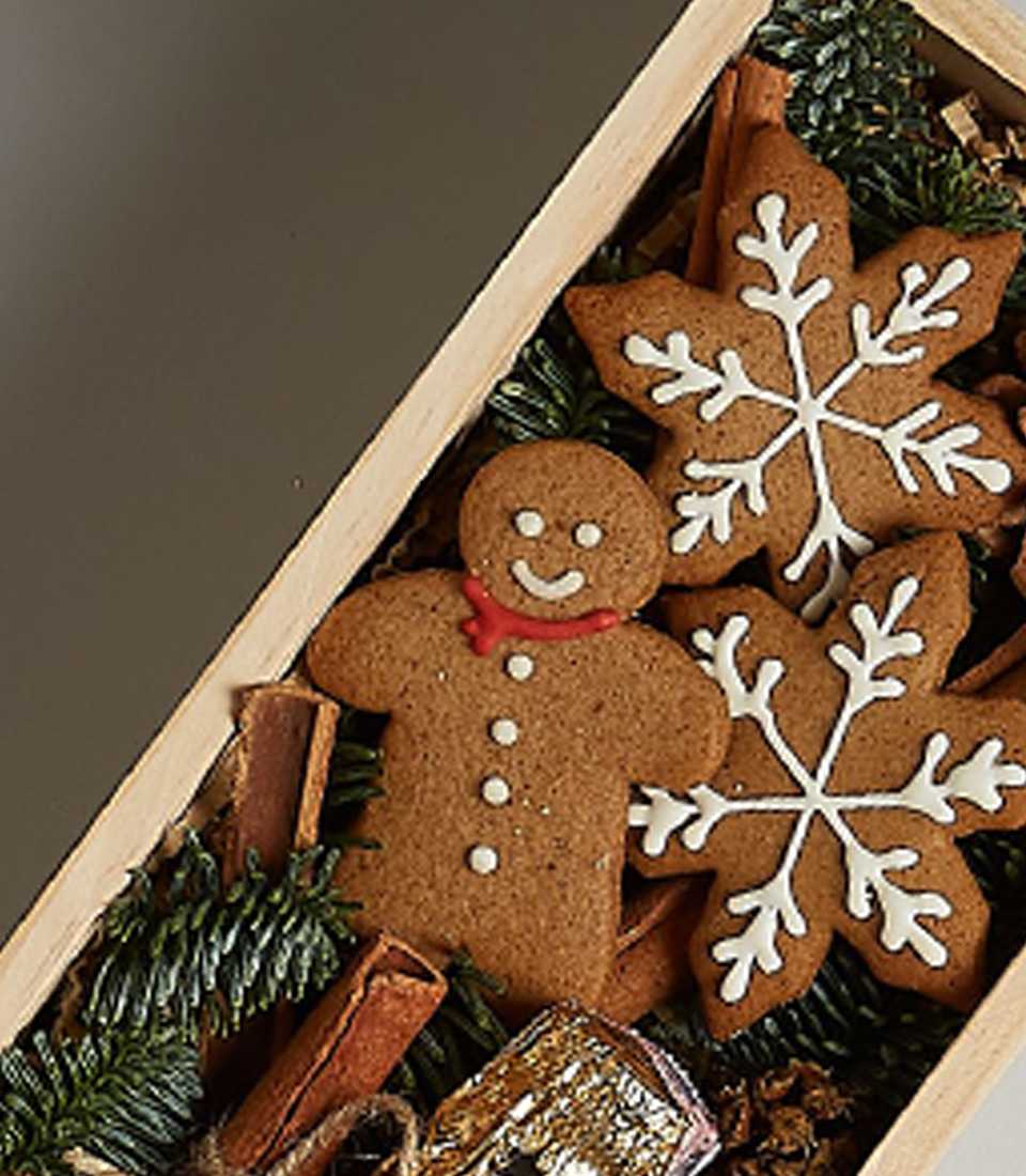 Holiday gift box with Moët & Chandon, gingerbread cookies, pinecones, and cinnamon sticks in a wooden container.