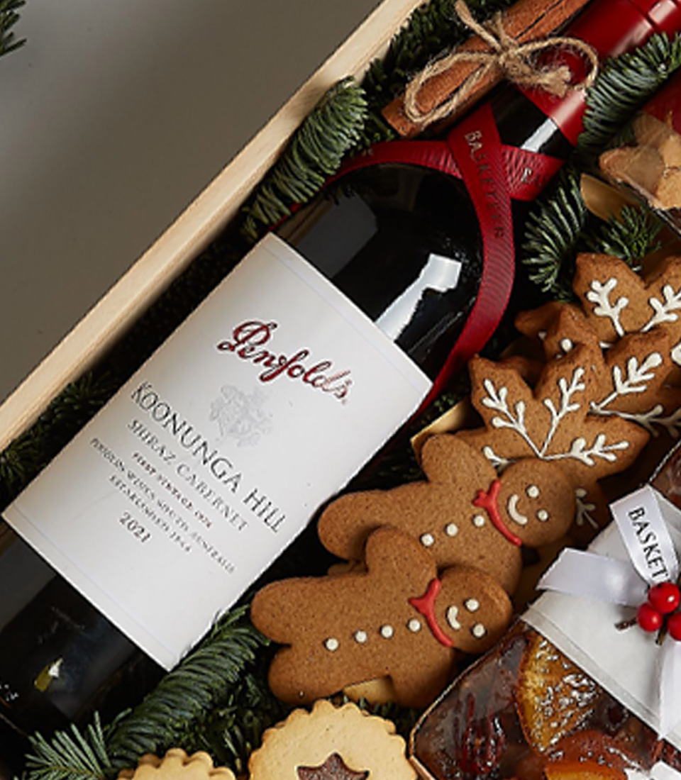 Gift box with Penfolds Koonunga Hill Shiraz Cabernet, gingerbread cookies, fruitcake, biscuits, chocolates, and festive decorations.