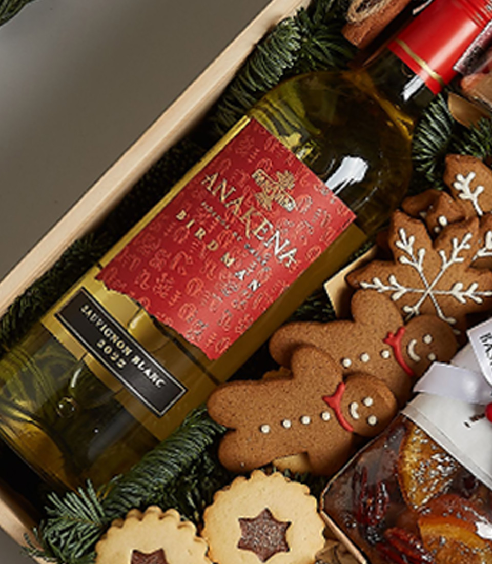 Holiday gift box featuring Anakena Sauvignon Blanc, gingerbread cookies, biscuits, chocolates, fruitcake, and festive decorations.