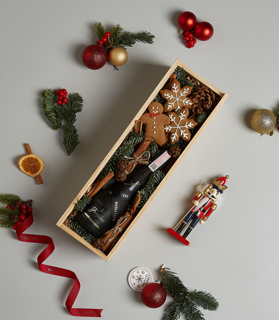 Holiday-themed gift box with Freixenet Prosecco, gingerbread cookies, and festive decorations in a wooden box.