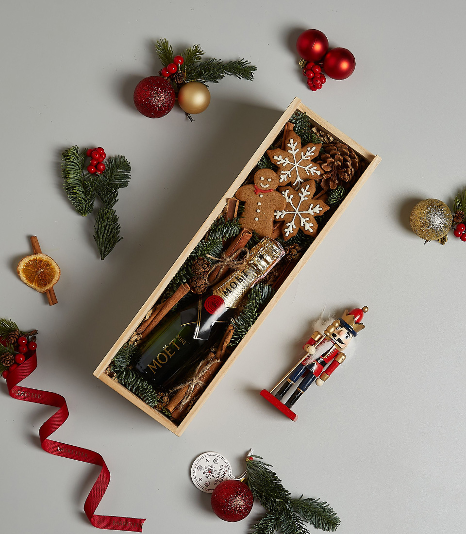 Holiday gift box with Moët & Chandon, gingerbread cookies, pinecones, and cinnamon sticks in a wooden container.
