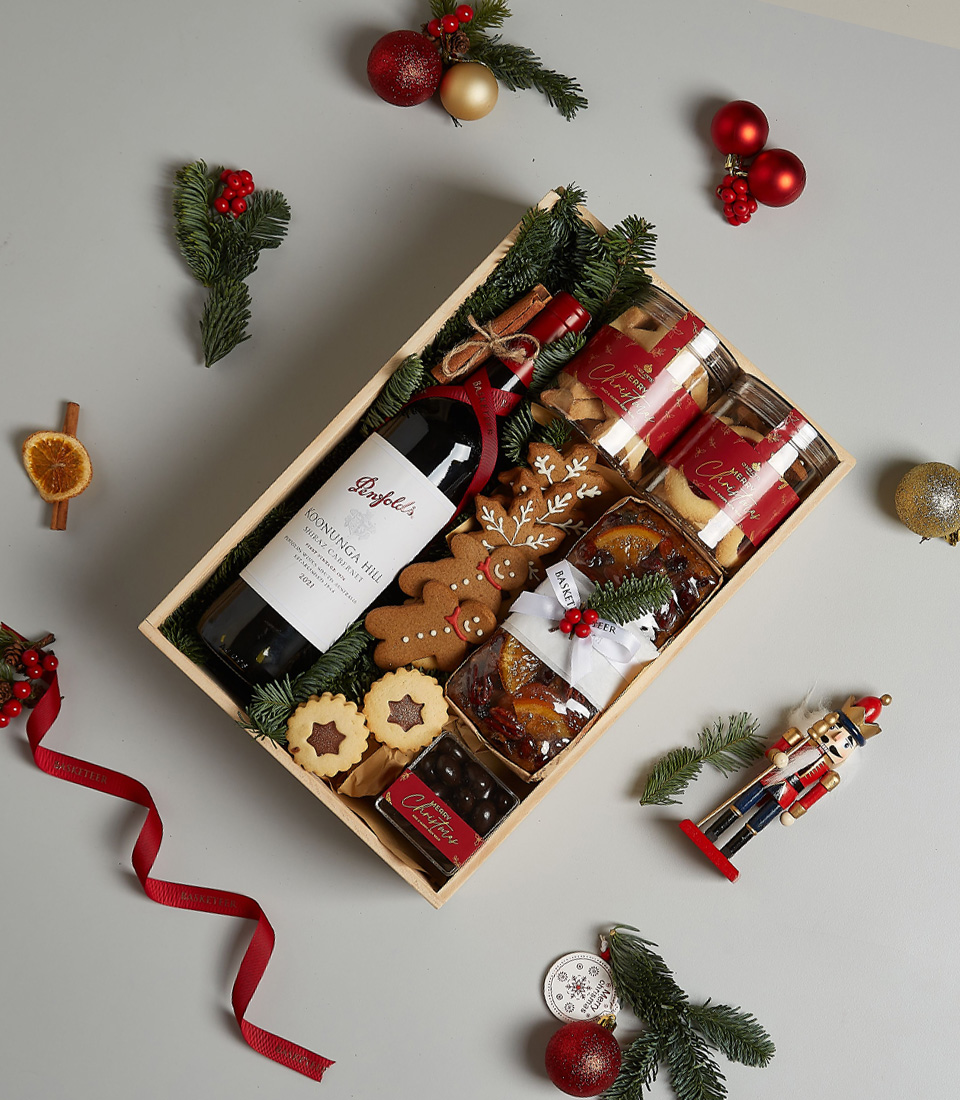 Gift box with Penfolds Koonunga Hill Shiraz Cabernet, gingerbread cookies, fruitcake, biscuits, chocolates, and festive decorations.