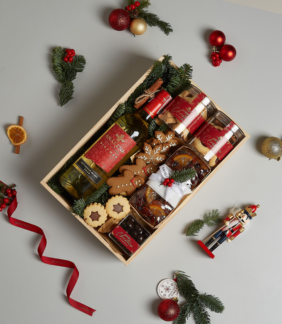 Holiday gift box featuring Anakena Sauvignon Blanc, gingerbread cookies, biscuits, chocolates, fruitcake, and festive decorations.