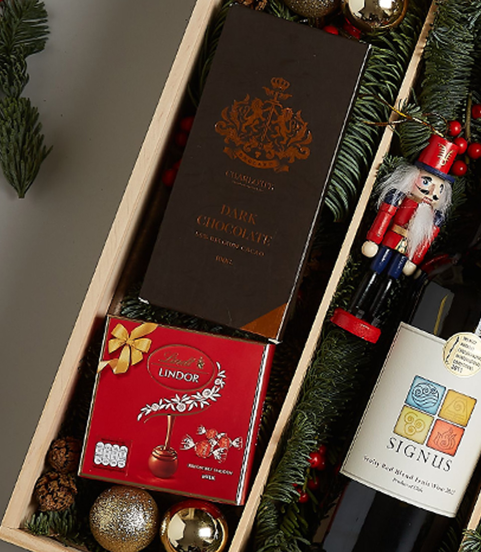 Holiday gift box with Signus wine, dark chocolate, Lindt pralines, festive cookies, and holiday decorations, elegantly packaged for Christmas celebrations.