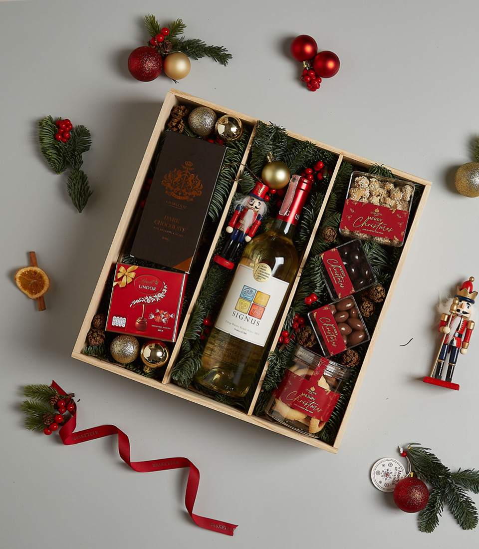 Christmas gift box with Signus white wine, dark chocolate, Lindt pralines, cookies, and festive decorations in an elegant arrangement.