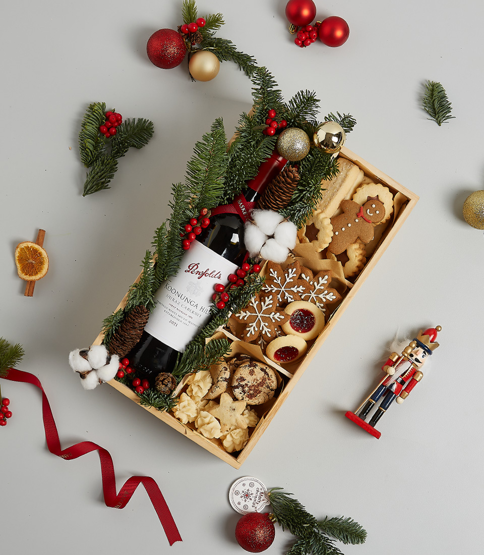 Christmas gift box featuring Penfolds red wine, festive cookies, gingerbread, snowflake treats, and holiday greenery decorations.