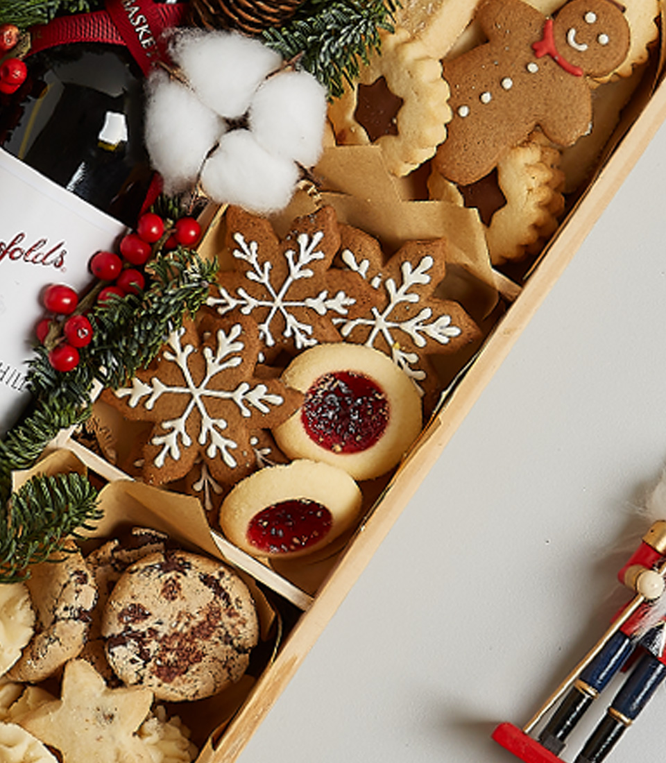 Christmas gift box featuring Penfolds red wine, festive cookies, gingerbread, snowflake treats, and holiday greenery decorations.