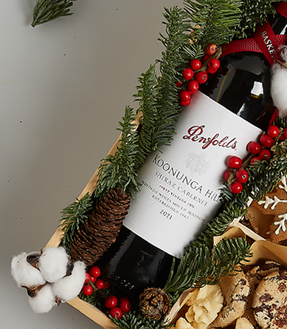 Christmas gift box featuring Penfolds red wine, festive cookies, gingerbread, snowflake treats, and holiday greenery decorations.