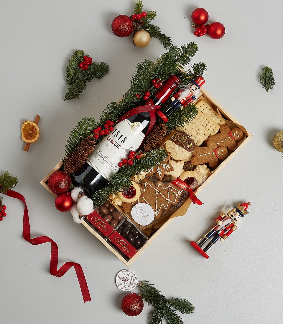 Festive gift box featuring Signus Classic Red Wine, cookies, gingerbread, and holiday-themed decorations, including greenery and nutcracker ornaments.